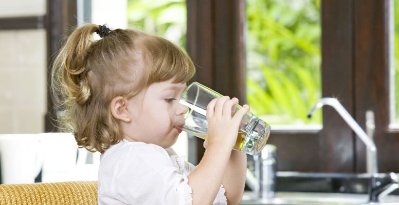 Little girl drinking water in kitchen