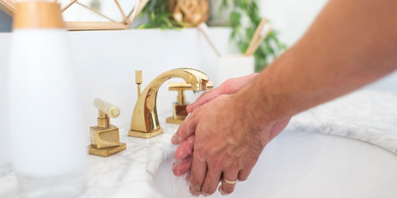 Man washing hands in sink with gold fixture